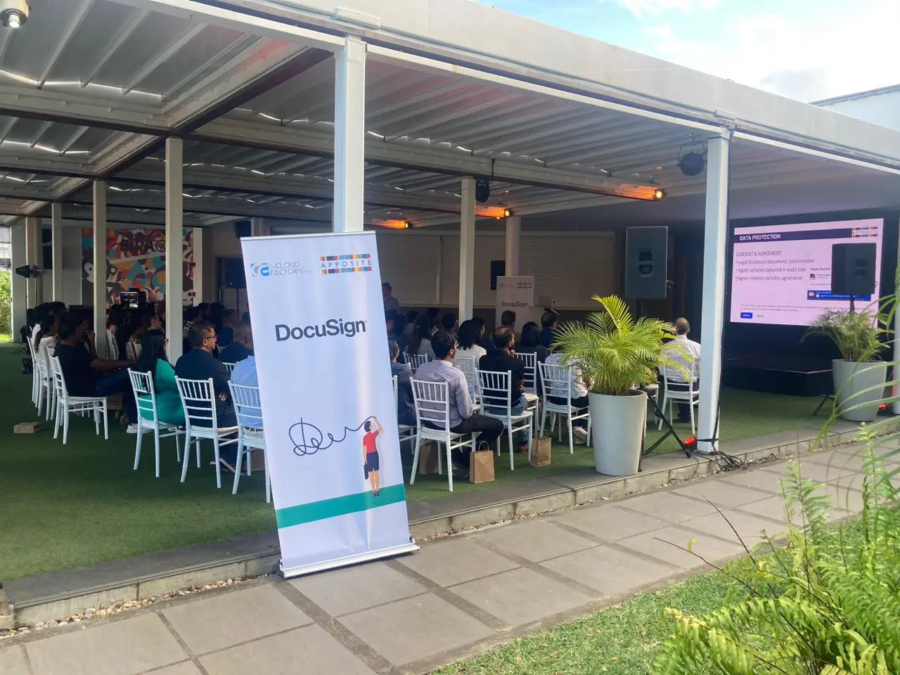 Outdoor event with attendees and presentation screen.