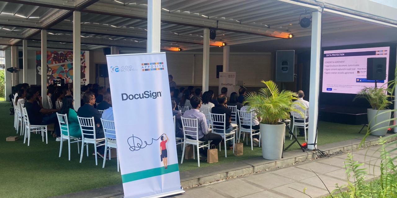 Outdoor event with attendees and presentation screen.